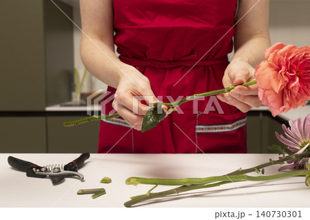 Florist removing excess leaves from flower stem at table. Hands cleaning plant preparing bouquet elements. Concept of floral arrangement preparation.. Florist removing excess leaves from flower stem at table. Hands cleaning plant preparing bouquet elements. Concept of floral arrangement preparation.. 140730301