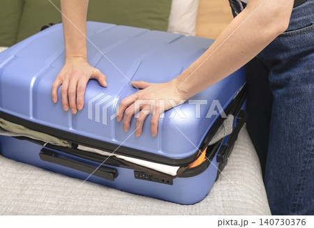 Person closing overfilled suitcase with force during packing process. Hands press lid on packed luggage. Concept of travel preparation overload organization.. 140730376