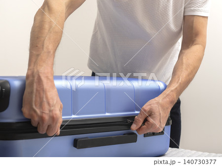 Person closing suitcase by pressing lid and holding handle during packing. Hands secure luggage before travel. Concept of preparation journey organization.. Person closing suitcase by pressing lid and holding handle during packing. Hands secure luggage before travel. Concept of preparation journey organization.. 140730377