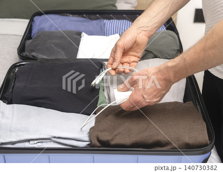 Person placing charging cable into suitcase while packing for trip. Hands organize electronic accessory inside luggage. Concept of travel preparation technology packing.. Person placing charging cable into suitcase while packing for trip. Hands organize electronic accessory inside luggage. Concept of travel preparation technology packing.. 140730382