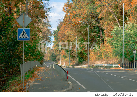 Autumn road lined with vibrant trees and pedestrian crossing sign Autumn road lined with vibrant trees and pedestrian crossing sign 140730416