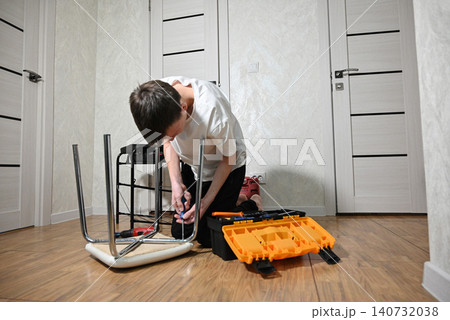 Young person working on stool assembly with tools in a home setting Young person working on stool assembly with tools in a home setting 140732038