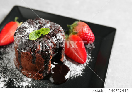 Delicious warm chocolate lava cake with mint and strawberries on plate, closeup Delicious warm chocolate lava cake with mint and strawberries on plate, closeup 140732419