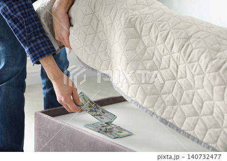 Man hiding dollar banknotes under mattress in bedroom, closeup. Money savings Man hiding dollar banknotes under mattress in bedroom, closeup. Money savings 140732477
