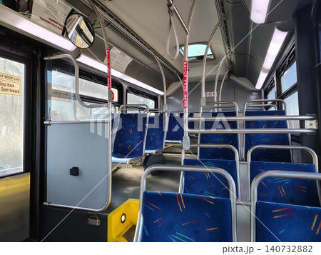 The interior of a public transit bus features multiple brushed stainless steel handrails and seats with a rigid metal frame and soft fabric upholstery in a rich blue color The interior of a public transit bus features multiple brushed stainless steel handrails and seats with a rigid metal frame and soft fabric upholstery in a rich blue color 140732882