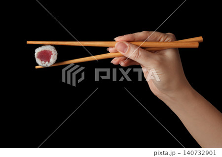 Woman holding sushi roll with chopsticks on black background, closeup Woman holding sushi roll with chopsticks on black background, closeup 140732901