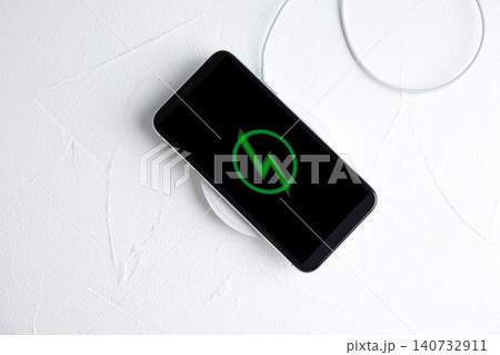 Mobile phone charging with wireless pad on white stone table, top view 140732911