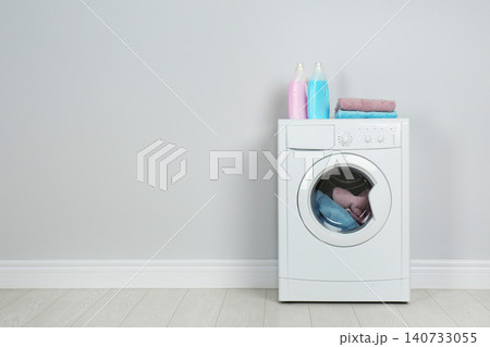 Modern washing machine with stack of towels and detergents near white wall, space for text. Laundry day 140733055