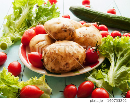 Portion of young potatoes and red ripe fresh cherry tomatoes, green lettuce, cucumber on table Portion of young potatoes and red ripe fresh cherry tomatoes, green lettuce, cucumber on table 140733292