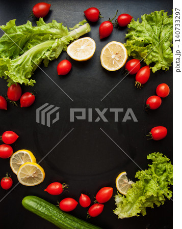 Frame made of red ripe fresh cherry tomatoes, green lettuce and cucumber on black background Frame made of red ripe fresh cherry tomatoes, green lettuce and cucumber on black background 140733297