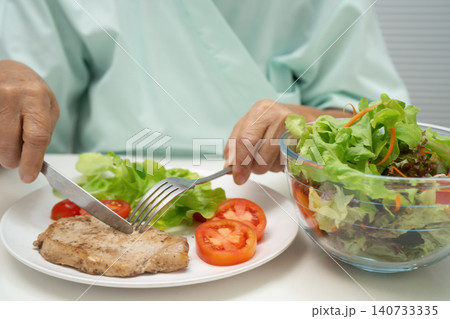 Asian elderly woman patient eating pork chop stake and vegetable salad for healthy food in hospital. Asian elderly woman patient eating pork chop stake and vegetable salad for healthy food in hospital. 140733335