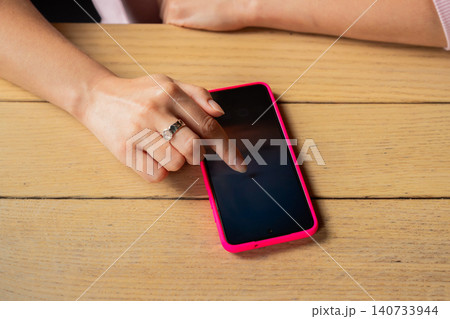 Woman using smartphone with pink case on desk. Girl clicking screen of mobile phone for social media and internet surfing. Digital lifestyle and communication concept with tech device. Woman using smartphone with pink case on desk. Girl clicking screen of mobile phone for social media and internet surfing. Digital lifestyle and communication concept with tech device. 140733944
