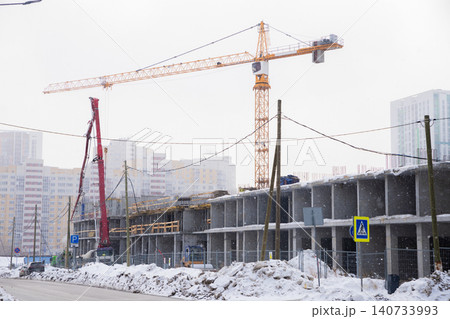 Tower crane at residential building construction site during winter snowfall. Concrete framework of unfinished house. Urban development project and architecture development industry concept. Tower crane at residential building construction site during winter snowfall. Concrete framework of unfinished house. Urban development project and architecture development industry concept. 140733993