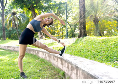 Asian woman relax after exercise in the garden with streching the body by lean on her right side and she look happiness. Asian woman relax after exercise in the garden with streching the body by lean on her right side and she look happiness. 140733997