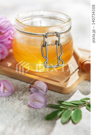 Acacia honey jar with blooming flowers and wooden dipper 140734108