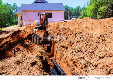 Heavy excavator works to create trench next to house during install drainage septic chamber pipe 140734262
