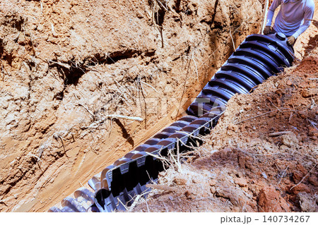 Workers lay down along septic drainage chamber pipe in trench at construction site Workers lay down along septic drainage chamber pipe in trench at construction site 140734267