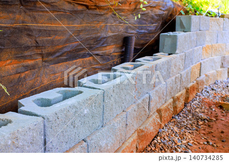 Workers are placing concrete blocks to build retaining wall in backyard area 140734285