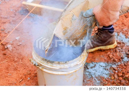 Worker holds bag, pours dry cement into bucket on construction site Worker holds bag, pours dry cement into bucket on construction site 140734338