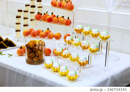 Dessert table features various sweets like cupcakes, cookies, decorative fruits at wedding event. Dessert table features various sweets like cupcakes, cookies, decorative fruits at wedding event. 140734345