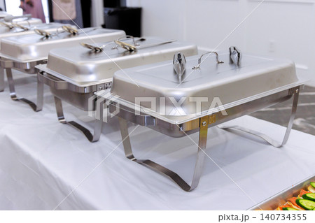 Chafing dishes sit on table ready for serving food during an wedding event at venue guests are expected soon. Chafing dishes sit on table ready for serving food during an wedding event at venue guests are expected soon. 140734355