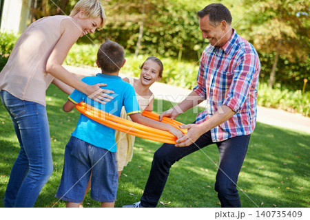 Parents, children and hula hoop in park as family, playing and bonding with motor skills outdoor. Kids, son and daughter with mother and father in nature for leisure, childhood development with smile 140735409