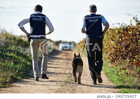 Policeman, dog and walk in field for crime scene or robbery with car for search, safety and law enforcement. Detective, investigation and uniform in outdoor working at countryside with gravel road Policeman, dog and walk in field for crime scene or robbery with car for search, safety and law enforcement. Detective, investigation and uniform in outdoor working at countryside with gravel road 140735427