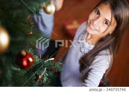 Portrait, child and smile by Christmas tree in home, festive season and happy to prepare for xmas. Female person, girl and care for decoration on religious holiday, celebration and love for tradition Portrait, child and smile by Christmas tree in home, festive season and happy to prepare for xmas. Female person, girl and care for decoration on religious holiday, celebration and love for tradition 140735740