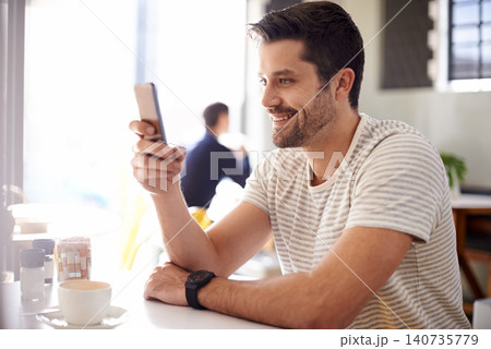Happy man, relax at cafe with smartphone and scroll online for social media, tech and communication. Chat, reading on app or ebook with break at coffee shop, contact and using phone with network Happy man, relax at cafe with smartphone and scroll online for social media, tech and communication. Chat, reading on app or ebook with break at coffee shop, contact and using phone with network 140735779