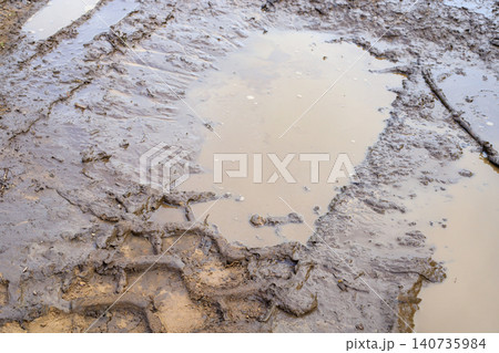 Muddy puddle with tractor tire tracks on winding dirt road, country lane lane with wet clay potholes landscape 140735984