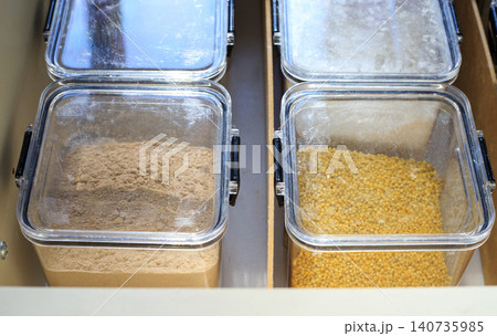 Food storage containers. White flour and long grain rice fill transparent plastic containers. Well-organized kitchen drawer storage contains various dry staples 140735985