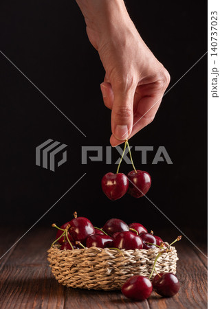 Hand picking fresh red cherries from a woven basket Hand picking fresh red cherries from a woven basket 140737023