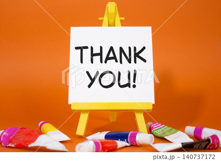 Thank you symbol. Wooden blocks with words Thank you. Beautiful orange background with paints and easel. Business and Thank you concept. Copy space. 140737172