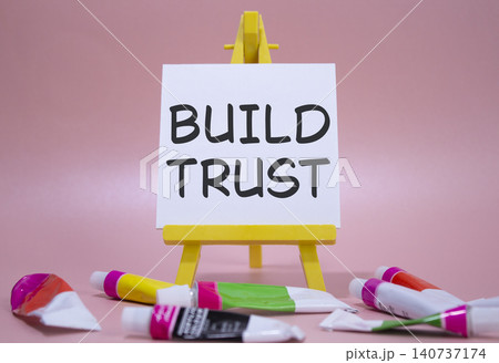 Build trust symbol. Wooden blocks with words Build trust. Beautiful pink background with paints and easel. Business and Build trust concept. Copy space. Build trust symbol. Wooden blocks with words Build trust. Beautiful pink background with paints and easel. Business and Build trust concept. Copy space. 140737174