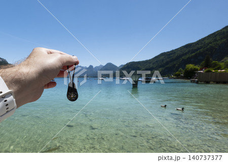 Hand holding a sportable compas over a clear lake with mountains in the background, presenting a compact outdoor exploration tool Hand holding a sportable compas over a clear lake with mountains in the background, presenting a compact outdoor exploration tool 140737377