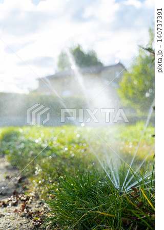 Concept of automated watering, efficient water management landscaping, gardening and sustainable lawn care. Sprinkler equipment distributes fine streams of water evenly over healthy turf, supporting Concept of automated watering, efficient water management landscaping, gardening and sustainable lawn care. Sprinkler equipment distributes fine streams of water evenly over healthy turf, supporting 140737391