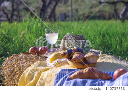 Picnic with wine glass and croissants on yellow blanket in orchard Picnic with wine glass and croissants on yellow blanket in orchard 140737858