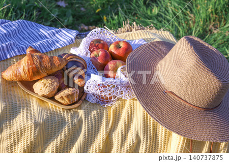 Picnic setup with bread, apples, and straw hat on yellow blanket Picnic setup with bread, apples, and straw hat on yellow blanket 140737875