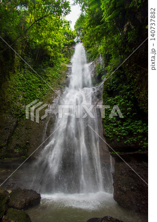 Majestic view of Coban Glotak waterfall hidden inside a lush tropical jungle on Mount Kawi, beautiful cascading water stream on a rocky cliff in Malang, Indonesia	 140737882