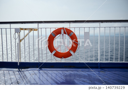 Bright orange life ring secured to a white ship railing with the open sea in the background, conveying safety, travel, marine and nautical calm on a clear sunny day. 140739229