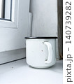 White simple mug with black rim rests on white windowsill. Signs of use with some marks on surface. Glass window, bright light, simple interior design 140739282