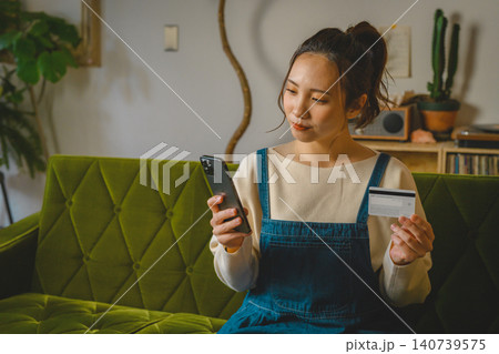 ソファでスマホとカードを持つ女性 140739575