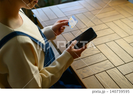 テーブルでスマホとカードを持つ手元 140739595