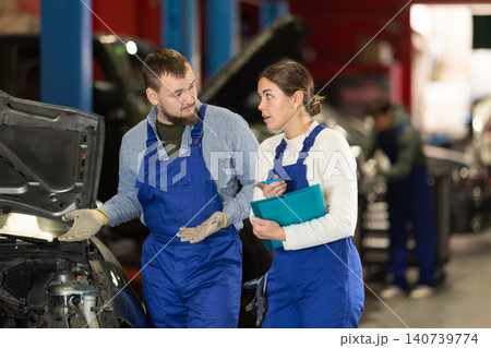 Car service manager discusses car repair problems with mechanic. He takes notes on paper Car service manager discusses car repair problems with mechanic. He takes notes on paper 140739774