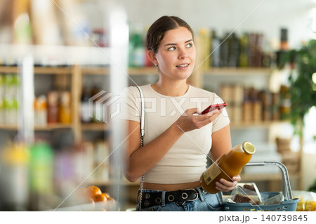European young woman customer at shop scans QR code on peach juice bottle using phone camera European young woman customer at shop scans QR code on peach juice bottle using phone camera 140739845