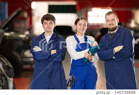 Team of auto mechanics, two men and one woman, wearing blue overalls and posing, ready to provide professional vehicle service 140739898