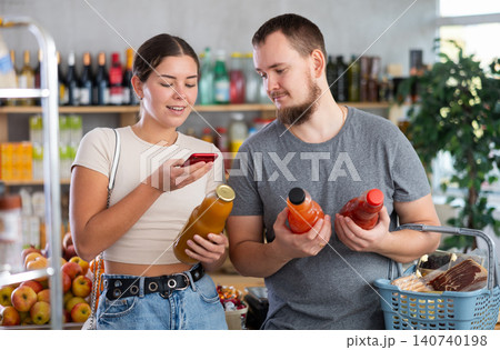 European spouses customer at shop scans QR code on juice bottle using phone camera 140740198