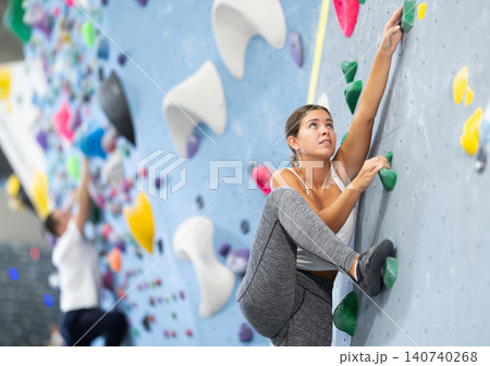 Sportive woman climbing on artificial rock wall in rock climbing gym Sportive woman climbing on artificial rock wall in rock climbing gym 140740268