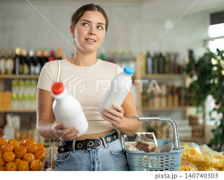 Girl hold packages bottles and choose consider milk in store Girl hold packages bottles and choose consider milk in store 140740303