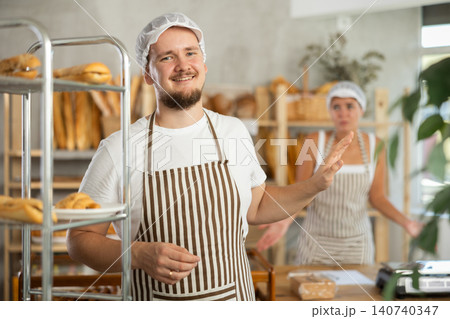 Content young man worker stands with his back to frustrated girl behind bakery counter 140740347